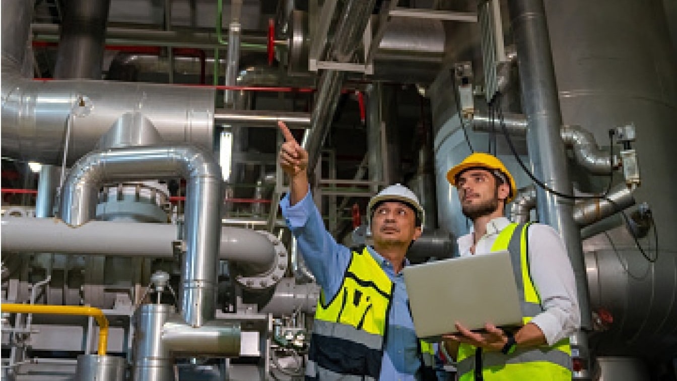 Two technicians reviewing piping in an industrial boiler room
