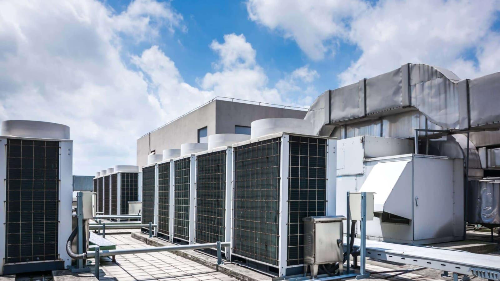 Row of commercial HVAC condenser units and ductwork on a building rooftop