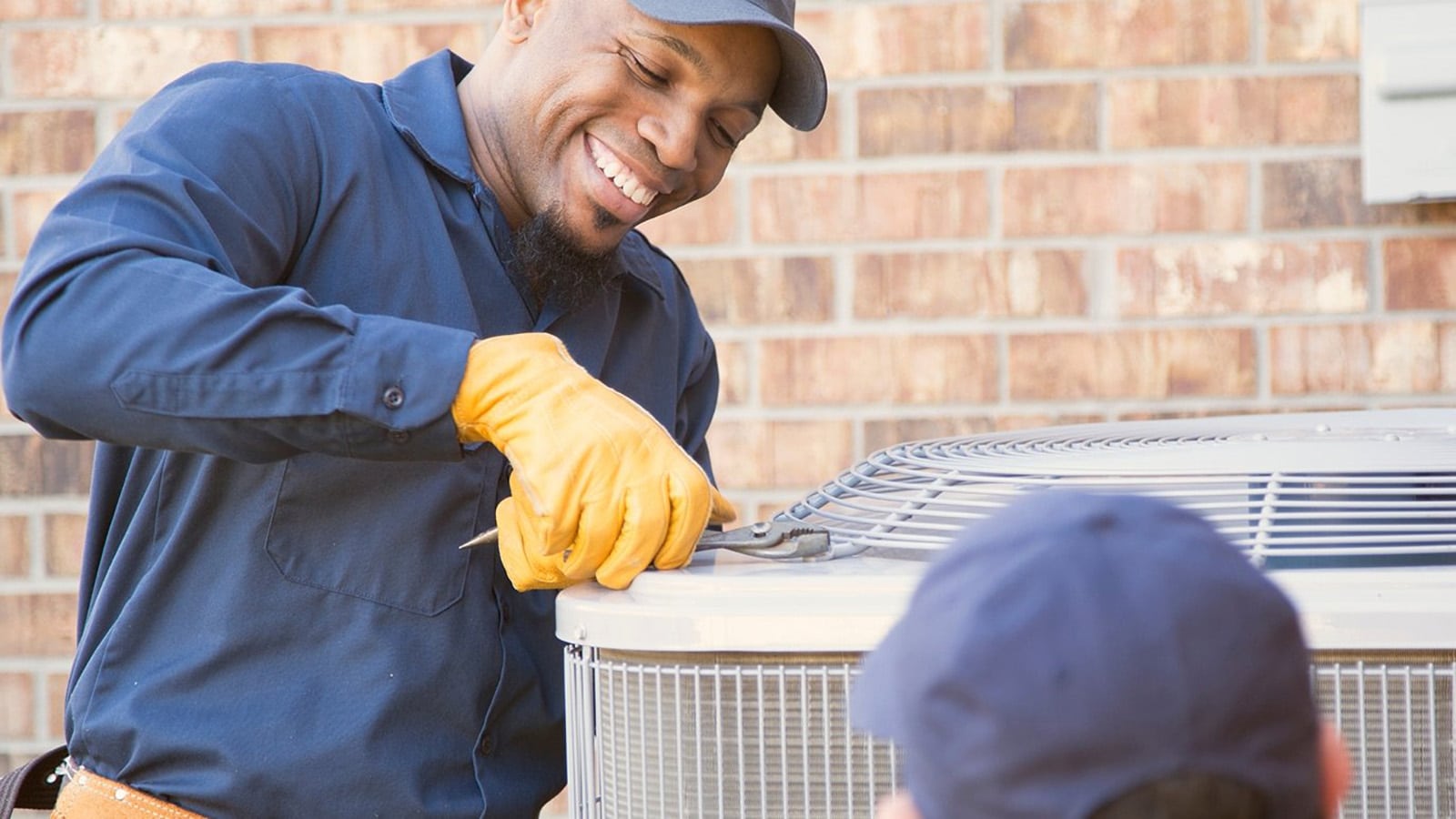 Smiling HVAC technician in gloves working on an outdoor condenser unit